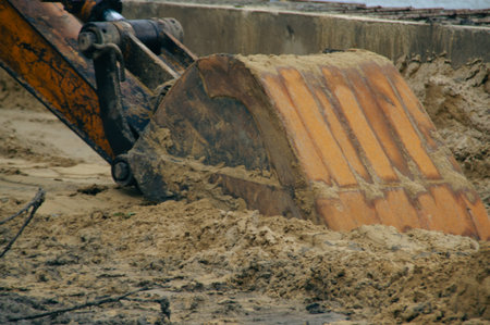 A close-up view of an excavator&#39;s bucket digging into sandy soil at a construction site.の写真素材