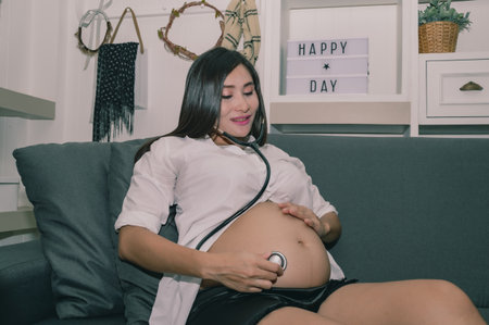Pregnant woman enjoying an intimate moment listening to her baby&#39;s heartbeat at home, showcasing maternal affection.の写真素材