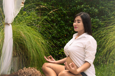 A woman meditating peacefully in a serene outdoor environment surrounded by lush greenery.の写真素材