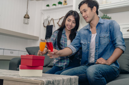 A happy couple enjoying drinks and gifts together, celebrating a special moment in their cozy living room.の写真素材