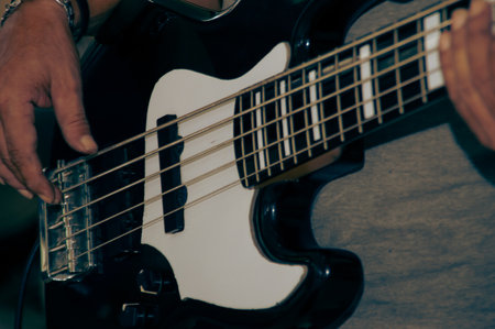 A close-up of hands playing a bass guitar, showcasing the instrument&#39;s unique design and vibrant details.の写真素材
