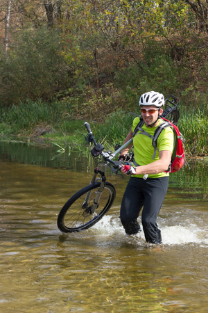 A man passes a river with a bicycle on his shoulder in a helmet and a backpack.の写真素材