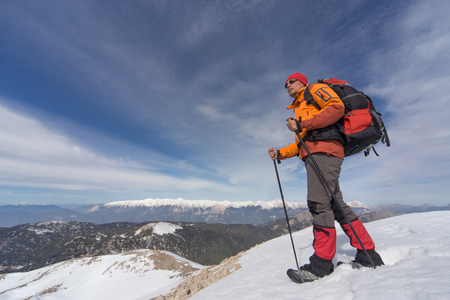 The young man with the backpack on top of a snow-covered mountain on a sunny day.の写真素材