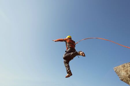 Man jumping off a cliff with a rope on a sunny day.