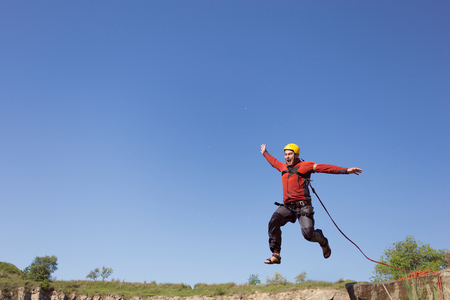 Man jumping off a cliff with a rope on a sunny day.