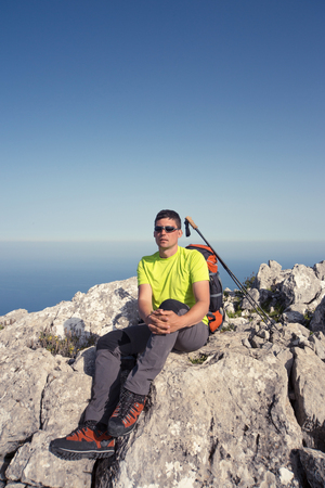 Young man with backpack on a mountain top on a sunny day.の写真素材