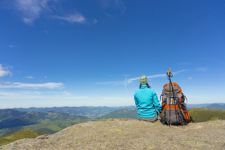 The girl in the campaign sitting on a rock in the mountains against the blue sky.の写真素材