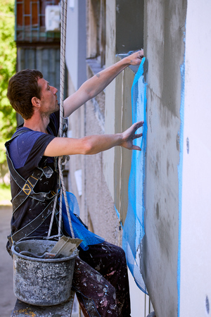 A man hanging on a rope performs work on the facade insulation.の写真素材