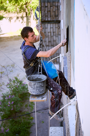 A man hanging on a rope performs work on the facade insulation.の写真素材