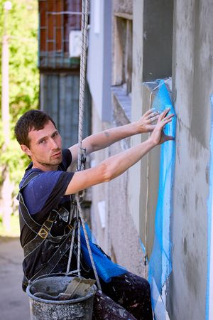A man hanging on a rope performs work on the facade insulation.の写真素材