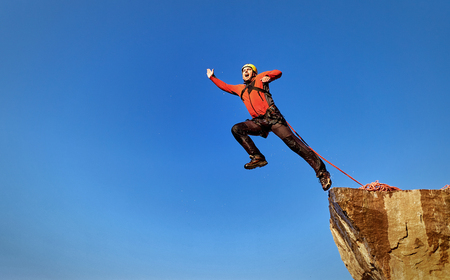 Man jumping off a cliff with a rope on a sunny day.