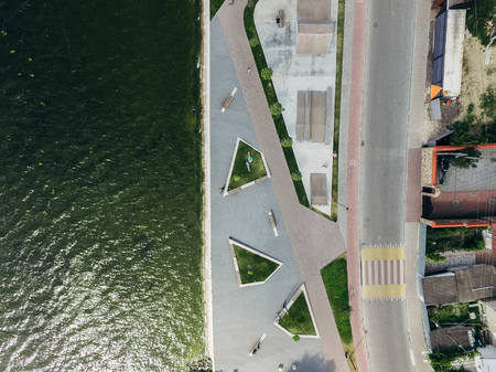 Aerial top view of the city embankment, road, lake, skate park. Two girls are lying on a green lawn. Surrealism.