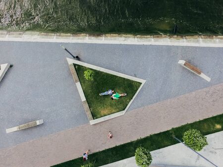Two girls are lying on a green lawn near a lake on the waterfront. Aerial view. Surrealismの写真素材