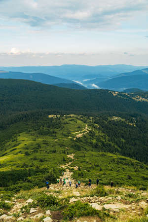 People descend down a large green mountain range. Mountain Hiking