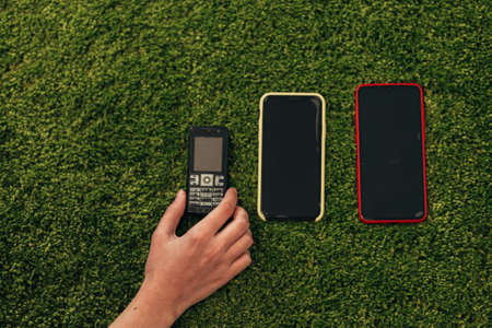 The Human Hand Picks an Old Phone That Lies Near New Smartphonesの写真素材