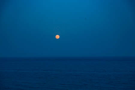 Full Red Moon Glows Brightly in the Blue Sky on a Evening Over the Seaの写真素材
