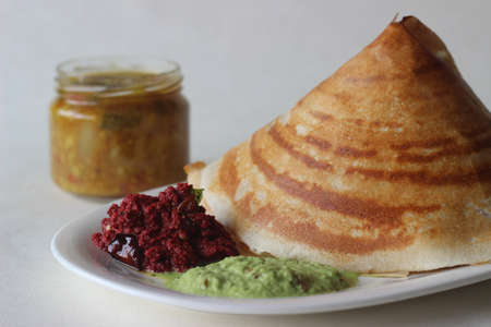 Crispy pancake made of rice and lentils folded in a cone shape. Served with spicy beetroot coconut condiments, coriander coconut condiments and sambar. Shot on white background.の写真素材