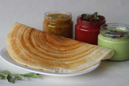 Crispy pancake made of rice and lentils. Served with spicy beetroot coconut condiments, coriander coconut condiments and sambar. Shot on white background.の写真素材