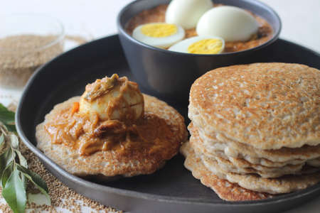 Kodo millet pancakes served with egg roast. Pancake is made with a fermented batter of kodo millet, flattened rice and coconut. Egg roast is Boiled egg in a spicy gravy of onions, tomatoes and spicesの写真素材