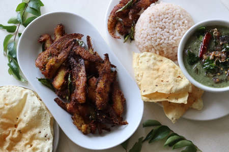 Crispy and spicy Anchovy fry. Anchovies marinated with spices and deep fried. Popular fish dish from Kerala called Natholi fry. Served with red rice meal along with papad. Shot on white background.の写真素材
