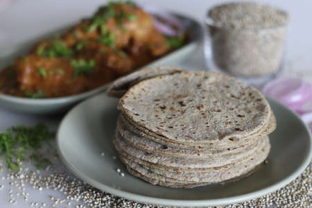 Soft flat bread made of pearl millet flour. Served with chicken in cashew gravy garnished with fresh coriander leaves. Shot on white background. Commonly called bajra roti and chicken curry in Indiaの写真素材