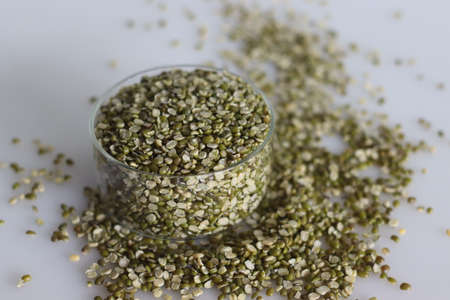Split moong bean lentils in a small glass bowl. Shot on white background with pile of split moong beans are scattered around.の写真素材