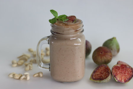 Fig Smoothie. Summer drink made of fresh fig in cashew milk, served in glass smoothie jar. Shot on white background along with fresh ripe figs and cashews around.の写真素材