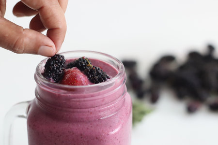 Mixed berry smoothie. Thick and creamy smoothie made of fresh strawberry and mulberry in almond milk. Served in smoothie jar. Shot on white background along with mulberries aroundの写真素材