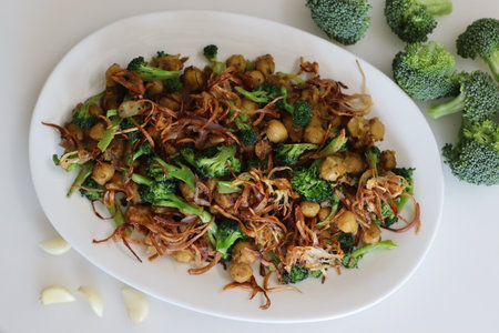 Chickpea broccoli stir fried. Garlic and broccolis stir fried with chickpeas, garnished with caramalised onions. A vegan food with healthy plant based protein. Shot on white backgroundの写真素材