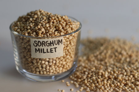 Closeup of sorghum millet grains kept in a glass bowl with label on it and filled to the brim, highlighting the tiny, golden grains with a rich earthy hue. Perfect for food and health related conceptsの写真素材