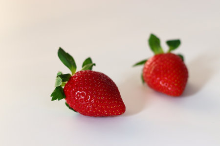 Two ripe strawberries with vibrant red color and fresh green leavesの写真素材