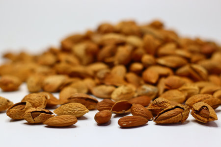 Raw almonds with shells scattered on a white surface, showcasing their natural texture and earthy tones. Packed with healthy fats, protein and vitamins, almonds support heart health and brain functionの写真素材