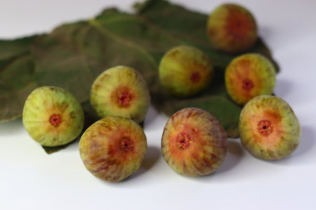 Fresh figs with green leaves on a white background. High in fiber, antioxidants, and vitamins, they aid digestion and support wellness. Ideal for food blogs, nutrition sites, and stock photographyの写真素材