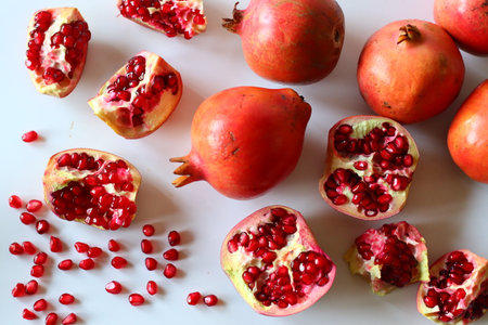 Pomegranate. Open fruit with glistening ruby red arils on a white surface, captured in soft natural...