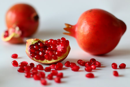 Pomegranate. Open fruit with glistening ruby red arils on a white surface, captured in soft natural lightの写真素材