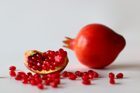 Pomegranate. Open fruit with glistening ruby red arils on a white surface, captured in soft natural lightの写真素材