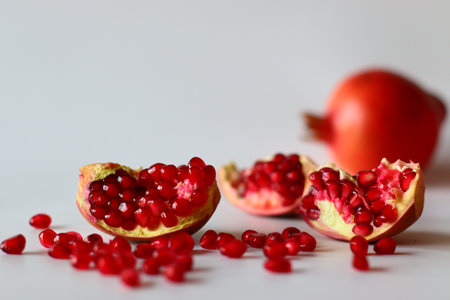 Pomegranate. Open fruit with glistening ruby red arils on a white surface, captured in soft natural lightの写真素材