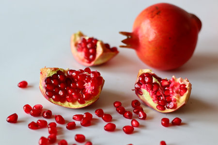 Pomegranate. Open fruit with glistening ruby red arils on a white surface, captured in soft natural lightの写真素材