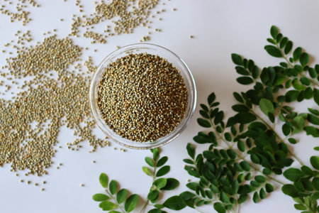 Fresh moringa leaves and a bowl of bajra or pearl millet set against a clean white backdropの写真素材
