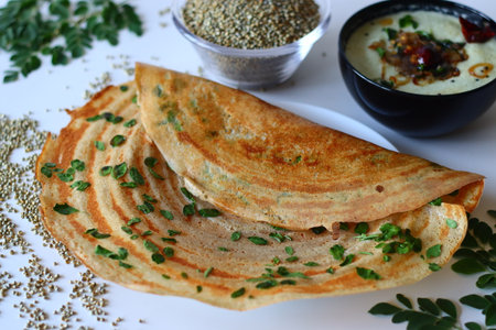 Bajra ghee dosa topped with fresh moringa leaves, served with spicy coconut chutney and rustic bowl...