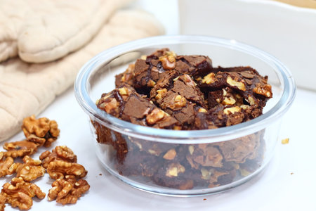 Rich, fudgy walnut chocolate brownie topped with crunchy walnut pieces, set on a bakery backdrop. A...