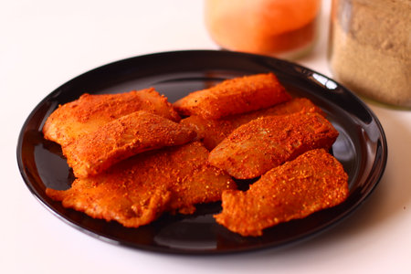 Raw tilapia fillets marinated in a bold Indian spice mix with red chili, turmeric, pepper, and salt, arranged on a black plate. Ideal for homemade fish curry, desi cuisine, or flavourful seafood prepの写真素材