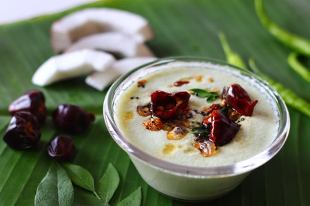 Two bowls of spicy coconut chutney, styled with coconut slices, green chilies, and curry leaves as props. A vibrant vegan friendly South Indian accompaniment good for Ayurvedic themed contenの写真素材