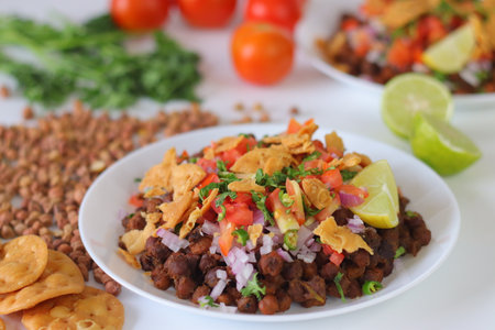 Chana Chaat with crushed papdi, topped with chickpeas, onions, tomatoes, chilies, coriander, and...