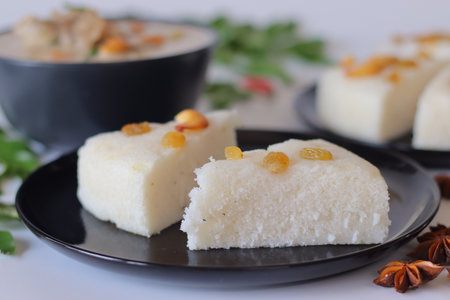 Kerala style vattayappam topped with golden raisins, sliced and served with mutton stew in coconut milk gravy. Styled with curry leaves, chilies, and star anise for a festive South Indian breakfast.の写真素材