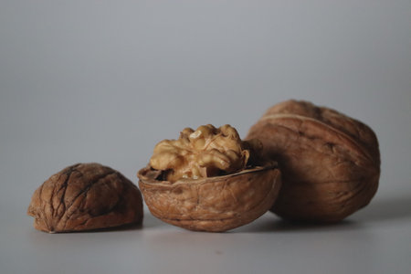 Walnuts presented in a minimal close up style, featuring one cracked open with visible kernel and...