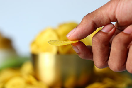 Banana chip presented in hand held style featuring a single thin and crisp yellow slice. A popular South Indian snack often enjoyed in Kerala. Ideal for themes of texture, snacking and culinary detailの写真素材