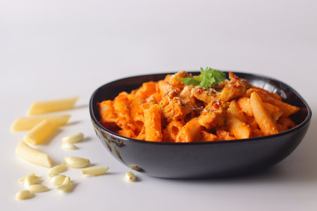 Red Sauce pasta. Creamy penne pasta in rich red sauce, topped with grilled chicken, chili flakes, and cilantro. Surrounded by raw pasta and garlic. Vibrant, appetizing food stylingの写真素材