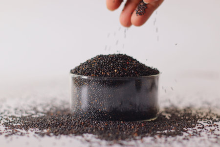 Black quinoa seeds pouring into a glass jar. Nutrient rich whole grain packed with protein and...