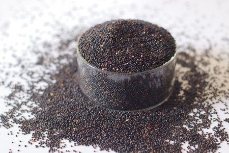 Black quinoa seeds in a glass bowl with scattered grains. Nutrient rich whole grain high in protein...